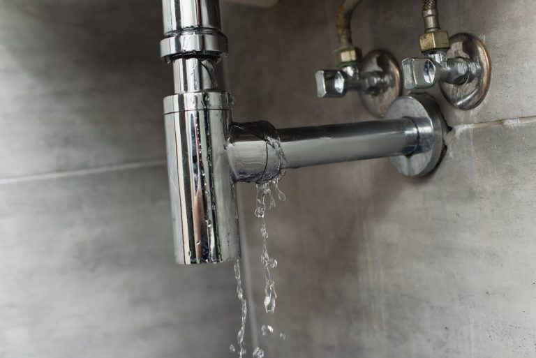 Damaged pipe with leaking water on grey background